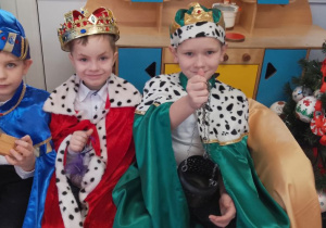 Trzech chłopców w roli Królów siedzi obok siebie. Dzieci trzymają kadzidło, złoto i mirrę.