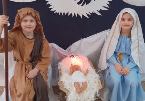 Antoś w roli Józefa i Marysia w roli Maryi siedzą przy żłóbku, w którym leży lalka (Jezusek).