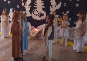 Marysia w roli Maryi i Antek w roli Józefa stoją przed Mikołajem w roli Gospodarza. W tle fragment dekoracji jasełkowej i dziewczynki w roli Aniołków oraz Gwiazdki