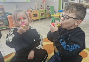 Weronika i Antoś wykonują ćwiczenia oddechowe z wykorzystaniem logopedycznych dmuchajek.