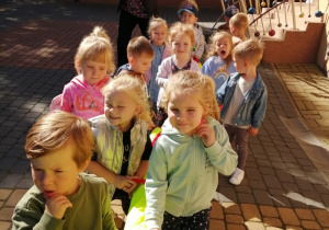 Dzieci stoją przed przedszkolem i trzymają kolorowego węża.