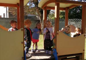 Grupka dzieci bawi się w pociągu, który znajduje się w ogrodzie przedszkolnym.