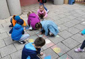 Dzieci malują kredą na tarasie przedszkolnym.