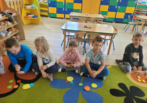 Dzieci z grupy "Biedronek" siedzą na dywanie. Przed sobą mają kolorowe kropki różnej wielkości, z których tworzą rozmaite obrazki.
