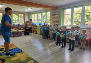 Dzieci z grupy "Biedronek" z piłkami w dłoniach słuchają poleceń instruktora.