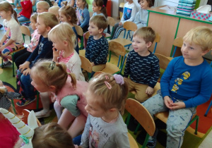 Dzieci siedzą na krzesłach i oglądają przedstawienie.