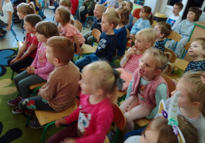 Przedszkolaki siedzą na widowni z uśmiechem na ustach.