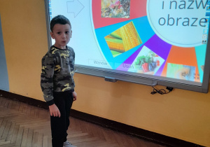 Igor stoi przed tablicą multimedialną. Chłopiec podczas gry "Jesienne koło fortuny" wylosował i nazwał obrazek przedstawiający muchomory.