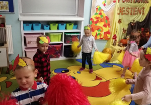 Dzieci w rozsypce na dywanie podczas tańca z czerwonymi i żółtymi pomponami.