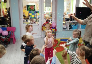 Dzieci stoją pod balonami, z których wylatują kolorowe konfetti.