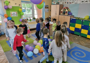 Dzieci z grupy "Słoneczka" spacerują między balonami po dywanie przy muzyce.