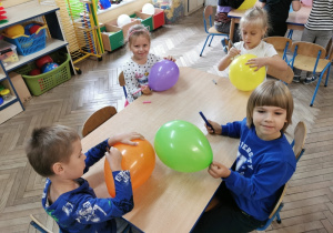Gabrysia, Natalia, Maksio i Oskar siedzą przy stoliku i ozdabiają swoje balony mazakami według własnych pomysłów.