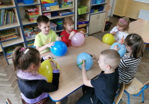 Wiktoria, Krzyś, Oliwia, Alicja, Alicja i Bruno siedzą przy stoliku i ozdabiają mazakami swoje balony.