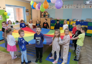 Dzieci wspólnie trzymają kolorową chustę animacyjną podczas zabawy w "Przebieganie pod chustą".