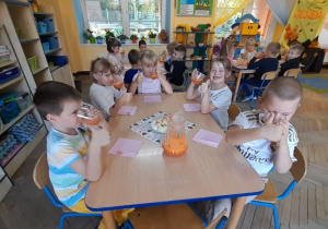 "Słoneczka" siedzą przy trzech stolikach i z apetytem piją sok jabłkowo-marchewkowy. Przy pierwszym stole dzieci podniosły kciuki do góry na znak, że sok im bardzo smakuje.