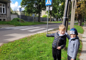 Fabian i Kacper pokazują pozostałym dzieciom znak przejścia dla pieszych.