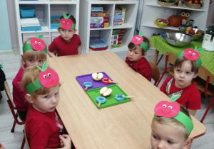 Grupka dzieci siedzi przy stole, na którym znajdują się dwie tacki z lupami i połówkami jabłek.