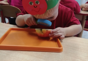 Wiktor siedzi przy stoliku i ogląda przez lupę przekrojone jabłko, które leży na pomarańczowej tacy.
