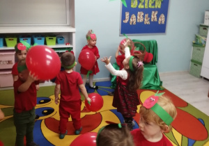 Wesoła zabawa przy muzyce na dywanie z czerwonymi balonami. W tle dekoracja z okazji Dnia Jabłka.