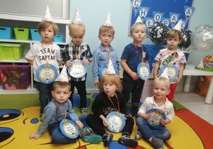 Zdjęcie grupowe chłopców w czapeczkach z medalami na tle dekoracji z okazji Dnia Chłopca.
