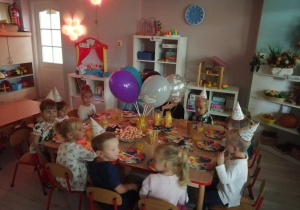 Dzieci siedzą przy wspólnym stole i ucztują z okazji Dnia Chłopaka.
