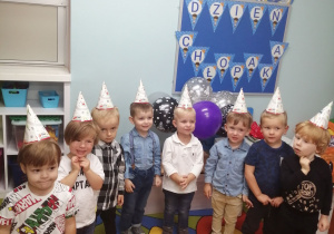 Zdjęcie grupowe chłopców w czapeczkach na tle dekoracji z okazji Dnia Chłopca.