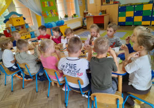 Dzieci siedzą przy złączonych stołach podczas wspólnego poczęstunku.