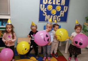 Zdjęcie zbiorowe dzieci w czapeczkach w uśmiechnięte minki z balonami.