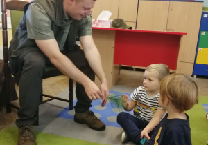 Pan leśniczy pokazuje dzieciom gałązkę jodły , którą dotyka Marcel.