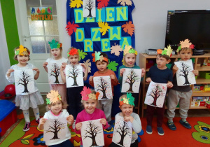 Grupa Motylków pozuje do zdjęcia z „jesiennymi drzewami”, za dziećmi – dekoracja.