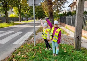 Alicja i Oliwia pokazują znak informacyjny "Przejście dla pieszych”.