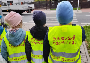 Troje dzieci obserwują przejście dla pieszych i działanie sygnalizacji świetlnej.