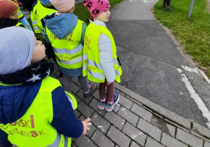 Przedszkolaki stoją na chodniku i oglądają oznaczenie ścieżki rowerowej