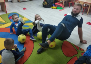 Grupka dzieci razem z trenerem wykonuje ćwiczenie z piłką.