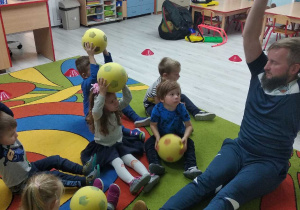 Grupka dzieci prezentuje ćwiczenie z piłką w górze.