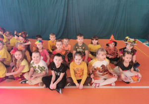 Dzieci z grupy Słoneczek siedzą po turecku i czekają na rozpoczęcie Balu jesiennego.