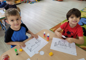 Eryk i Tymek siedząc przy stolikach tworzą prace matematyczno – plastyczną.