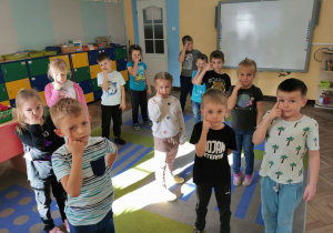 Dzieci stoją na dywanie w trakcie zabawy "Prawa - lewa" i pokazują swoje prawe oko.