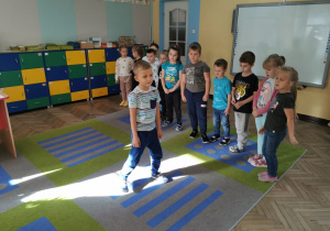 Hubert T. bierze udział w zabawie "Chodzenie pod dyktando". Pozostałe dzieci bacznie obserwują czy poprawnie wykonuje polecenia nauczyciela.