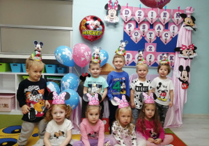 Zdjęcie grupowe dzieci w czapeczkach Myszki Mickey na tle dekoracji z okazji Dnia Postaci z Bajek.