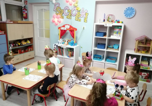 Dzieci siedzą przy stolikach i kolorują bajkowe kolorowanki z Myszką Mickey.