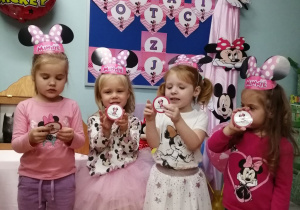 Grupka dziewczynek pozuje do zdjęcia na tle dekoracji z otrzymanymi odznakami Myszki Mickey.