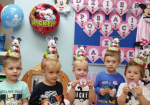Grupka chłopców pozuje do zdjęcia na tle dekoracji z otrzymanymi odznakami Myszki Mickey.