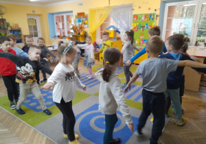 Dzieci poruszają się w kole na dywanie naśladując lot samolotem przy piosence pt. "Witajcie w naszej bajce".