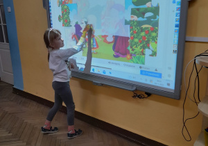 Oliwia stoi przed tablicą multimedialną i układa puzzle "Jaś i Małgosia".