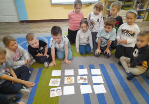 Przedszkolaki siedzą na dywanie, a na środku leżą obrazki. Dzieci grają w grę "Memory bajkowe".