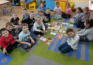 Dzieci siedzą na dywanie, a na środku leżą obrazki bajek oraz dopasowanych do nich rekwizytów. "Słoneczka" prezentują wykonane przez siebie zadanie.