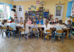 Dzieci siedzą przy połączonych stołach i wykonują kartę pracy pt. "Zaprowadź Jasia i Małgosię do piernikowego domku".