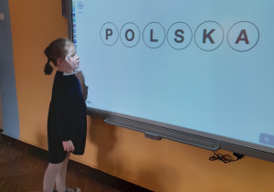 Alicja czyta ułożone na tablicy multimedialnej słowo - Polska.