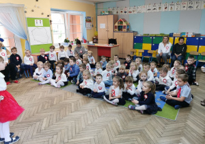 Przedszkolaki siedzą na dywanie i oglądają występ w wykonaniu dzieci z grupy "Słoneczka".